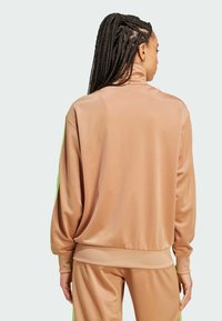 Hellebraune Sportjacke aus glattem Stoff mit grünen Seitenstreifen und hohem Kragen. Lockere Passform mit gerippten Bündchen und Saum.