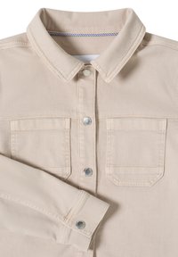 Veste en jean beige avec col pointu, deux poches à rabat sur la poitrine, et fermetures à boutons-pression sur le devant et aux poignets.