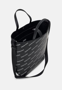 Svart toteväska med en texturerad yta. Utrustad med tryckt "Tommy Jeans"-logotyp, dubbla handtag och ett rymligt inre.