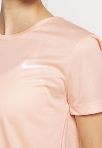 Lichtroze sport-T-shirt gemaakt van gladde stof, met een wit Nike-logo op de linkerborst en korte mouwen.