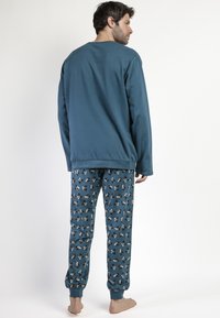 Conjunto de pijama para hombre con una camiseta de manga larga en color verde azulado y pantalones azules con un patrón que presenta pequeños gráficos de animales, puños elásticos y un corte relajado.