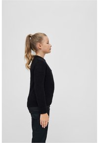 Maglione nero lavorato a maglia con maniche lunghe, scollatura rotonda e finitura testurizzata. Abbinato a pantaloni cargo scuri. Vista di profilo.
