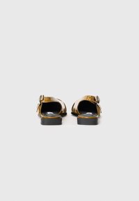 Brown patent leather sandals with an open back, ankle strap, and small heel. Features a metallic buckle accent and smooth texture.