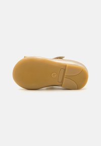 Sole di scarpa color tan con texture rigata, caratterizzata da un bordo superiore liscio. Materiale in gomma resistente con segni circolari e una stampa del logo.