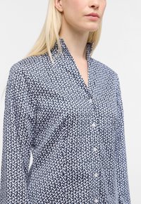 Camicia a maniche lunghe in navy e bianco, con un design geometrico, colletto e dettagli con bottoni.