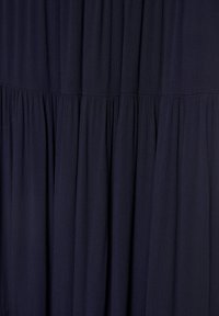 Sötét tengerészkék szövet összegyűrt, réteges textúrával, amely lágy, függőleges redőket és finom vízszintes varrási részleteket hoz létre.