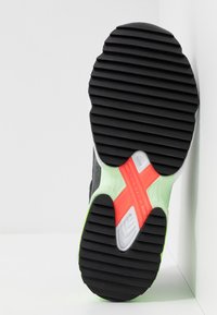 Musta kuminen urheilusneakerin pohja, jossa on teksturoitu pinnan kaarros, ja neonvihreitä sekä punaisia yksityiskohtia. Keskellä on valkoinen TORSION-logo.