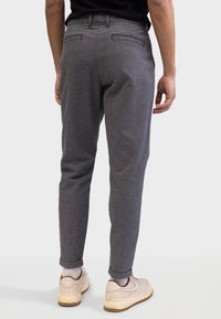 Szare spodnie w jodełkę o slim fit, z podwiniętymi nogawkami i dwiema tylnymi kieszeniami, w zestawie z beżowymi trampkami.
