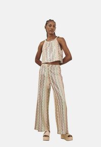 Conjunto de dos piezas que incluye un Top corto con lentejuelas y un pantalón de pierna ancha, que presenta un patrón ondulado en colores pasteles. Combinado con sandalias de plataforma.