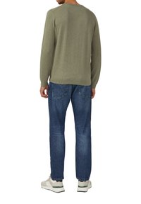 Grüner Strickpullover mit gerippten Bündchen, kombiniert mit blauen Jeans. Die Turnschuhe haben ein beige-grünes Design. Rückansicht von über der Taille.