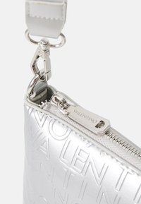 Clutch metallico argento con logo impressionato, chiusura a zip e cinturino regolabile. Presenta una texture liscia e un evidenza di hardware prominente.
