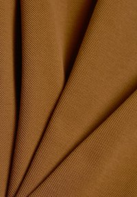 Tissu texturé de couleur marron avec un motif tissé, présentant de multiples plis créant de la dimension et de la profondeur. Le matériau semble durable et robuste.