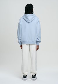Sudadera azul claro con capucha ajustable, corte relajado, puños acanalados, combinada con pantalones de chándal blancos y zapatillas negras.
