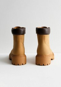 Stivali alla caviglia in pelle color tan con un colletto imbottito marrone, suola spessa a tasselli e dettagli cuciti. Il design presenta una punta arrotondata e una texture liscia.