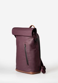 Zaino roll-top di un profondo viola con una texture liscia, dotato di una tasca frontale con zip e dettagli in pelle marrone alla base e sulle cinghie.