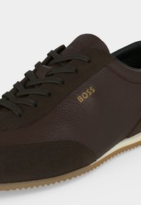 Baskets en cuir marron foncé avec lacets noirs, côtés texturés et marquage "BOSS" en doré sur le côté extérieur près des lacets.