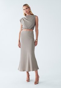 To-delt tøj sæt i lys beige, bestående af en draperet, kortærmet bluse og en tætsiddende, ankel-længde nederdel med en glat tekstur.