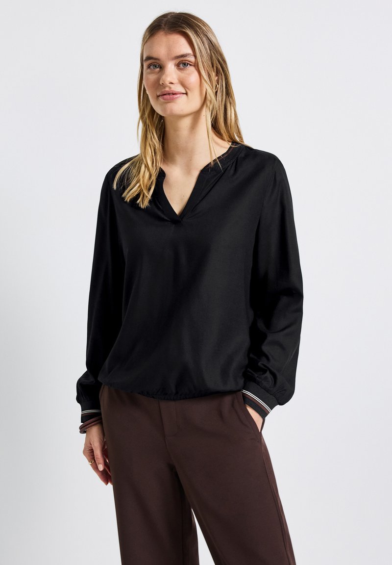 Schwarze Bluse mit langen Ärmeln und V-Ausschnitt, lockere Passform und elastischem Saum. Die Manschetten haben ein gestreiftes Akzentdetail.