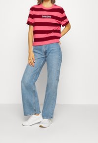 Short-sleeve, cropped t-shirt in pink and burgundy stripes with "Tommy Jeans" logo. Paired with light blue wide-leg jeans and white sneakers.