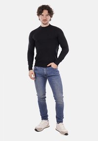 Maglione nero a maniche lunghe con collo alto abbinato a jeans skinny azzurri e sneakers bianche, caratterizzato da un design attillato e una texture liscia.