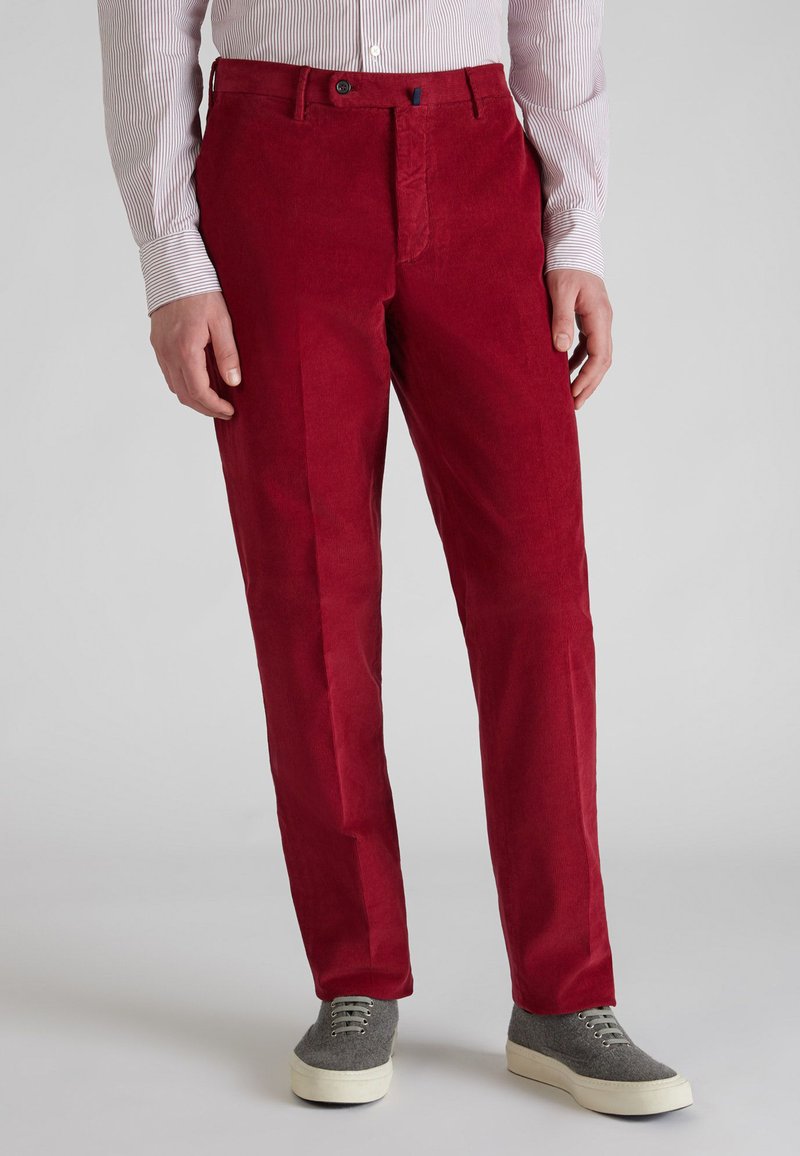 Pantalones de pana rojos con un corte recto, que cuentan con cierre de botón y bolsillos frontales. Combinados con una camisa de manga larga a rayas claras y zapatos grises.