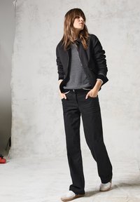 Veste zippée noire par-dessus un pull à motifs noir et blanc, associée à un jean large noir et des baskets blanches. Texture lisse, coupe décontractée.