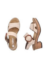 Sandales beige avec deux larges brides, talon en liège, boucle accent circulaire marron et semelle en cuir de couleur tan. Comprend des détails de couture sur les brides.