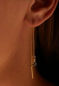 Gouden kettingoorbellen met een hangend ontwerp, voorzien van een zwarte steenaccent en drie kleine heldere stenen, die elegantie en detail benadrukken.
