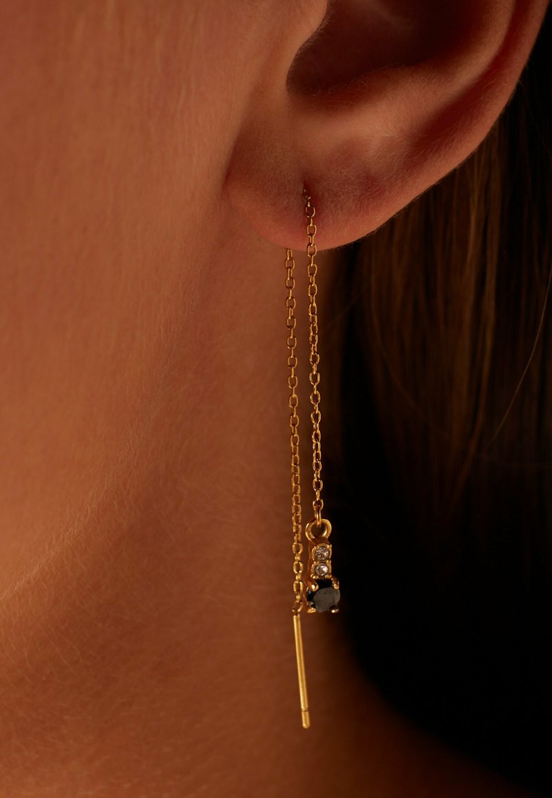 Gouden kettingoorbellen met een hangend ontwerp, voorzien van een zwarte steenaccent en drie kleine heldere stenen, die elegantie en detail benadrukken.