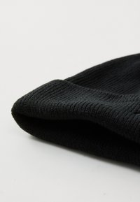 Nærbilde av en brettet svart strikket lue, som viser det teksturerte stoffet og den rullede kanten mot en nøytral bakgrunn.