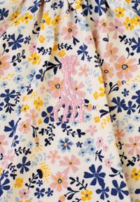 Tessuto a fantasia floreale con fiori gialli, rosa e blu su sfondo crema; presenta un dettagli ricamato di giraffa rosa.