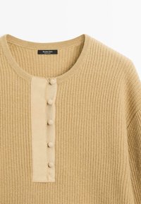 Beige gebreide trui met een ronde hals, gestructureerde stof en een knopenlijst aan de voorkant met vijf met stof overtrokken knopen.