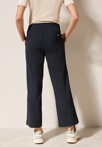 Pantalones de pierna ancha azul marino con una tela texturada y una cintura elástica, que cuentan con bolsillos traseros y se combinan con zapatillas ligeras.