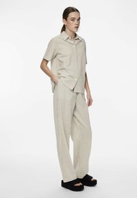 Camicetta a maniche corte a righe beige e pantaloni a vestibilità ampia in tessuto coordinato; indossato con sandali con piattaforma neri. Design e texture minimalisti.