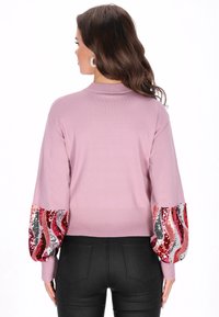 Różowy sweter z ribbowanym wykończeniem i długimi rękawami, ozdobiony cekinowym wzorem fal w czerwonym, srebrnym i różowym kolorze na rękawach.