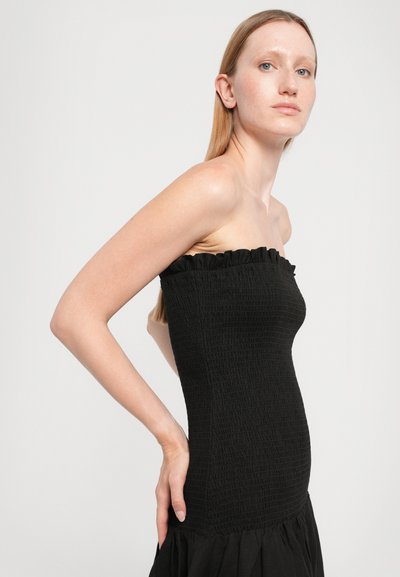 Juoda vamzdelio formos suknelė su tekstūruotu raukinimu ir raukšlėtu viršutiniu kraštu, su aptempta liemenėle ir platėjančia, susiraukšlėjusia sijonu.