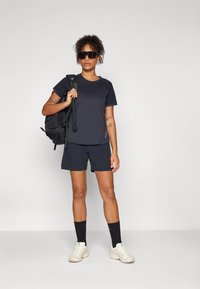 Marineblå trenings t-skjorte og shorts, laget av fukttransporterende stoff. Svart ryggsekk, hvite joggesko, lange svarte sokker med detaljer.