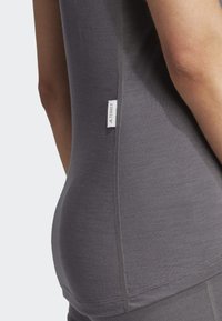 Gray athletic top made of soft material, featuring a slim fit, stitching details, and a small tag on the side.