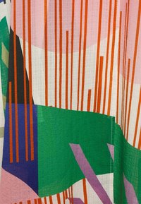 Flerfärgad tyg med djärva mönster i rosa, grönt, blått och orange sektioner, samt vertikala orange ränder på en texturerad bakgrund.