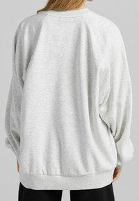 Sudadera gris clara de corte relajado, con mangas raglán y puños acanalados. Textura suave, dobladillo fruncido y sin logotipos ni patrones visibles.