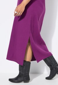 Vestido largo texturizado morado con una abertura lateral, acompañado de botas vaqueras negras de punta afilada con detalles florales.