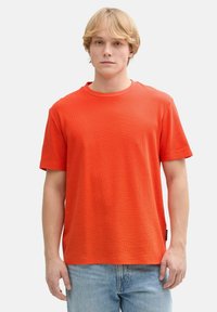 Rød kortærmet t-shirt med rund hals lavet af struktureret stof, parret med lyseblå denim jeans, der har en afslappet pasform uden synlige mønstre.