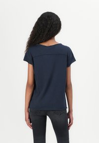 Námořnická modrá tričko s krátkým rukávem a kulatým výstřihem s kontrastním panelem na zadní straně. Měkká, lehká tkanina s volným střihem.