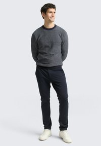 Grauer strukturierter Pullover mit einem navyblauen Rippkragen, kombiniert mit navyblauen eng anliegenden Hosen und weißen Sneakers. Schlichtes Design und neutrale Farben.