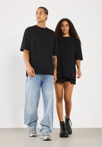 Svarte oversized t-skjorter med korte ermer, løse denimjeans og teksturerte svarte platåstøvler. Modellens stil er uformell og avslappet.