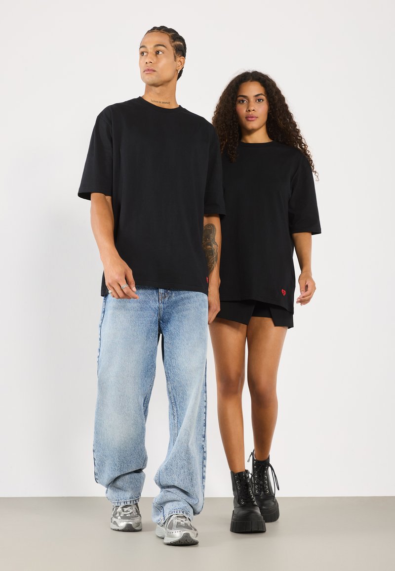 Svarte oversized t-skjorter med korte ermer, løse denimjeans og teksturerte svarte platåstøvler. Modellens stil er uformell og avslappet.