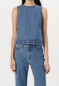 Top sin mangas de mezclilla azul, con un diseño ligeramente corto, que presenta un escote redondo y dobladillo deshilachado, combinado con jeans de tiro alto a juego.