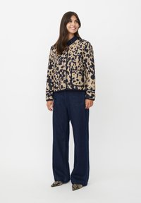 Giacca in stampa leopardata beige e nera, con chiusura a zip, due tasche anteriori e polsini a costine. Abbinata a jeans scuri a gamba larga.