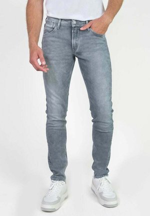 Jeans de mezclilla gris con corte ajustado, con un acabado desgastado, cinco bolsillos y un cierre clásico de botones. Combinados con zapatillas blancas.