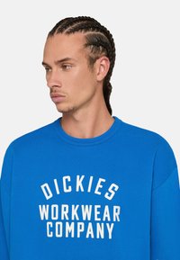Sudadera azul de mezcla de algodón, con cuello redondo, puños acanalados y un gran logotipo impreso en blanco que dice "DICKIES WORKWEAR COMPANY."